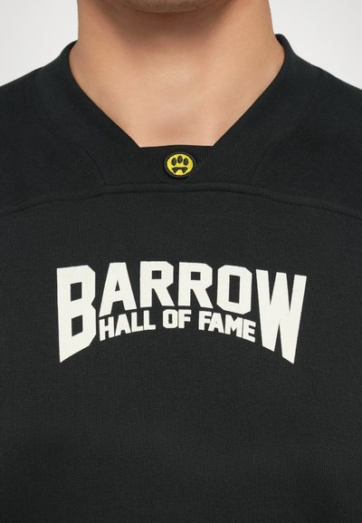 Sudadera de cuello redondo negra con un texto blanco en negrita que dice "BARROW HALL OF FAME" y un logotipo amarillo con una huella en el cuello.