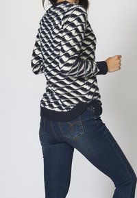 Námořnický a krémový pletený svetr s vlnovým vzorem, s dlouhými rukávy a žebrovanými manžetami. V kombinaci s tmavě modrými skinny džíny.