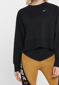 Zwarte cropped sweatshirt met lange raglanmouwen en een wit Nike-logo. Gecombineerd met strakke gouden leggings met witte tekst en accenten.