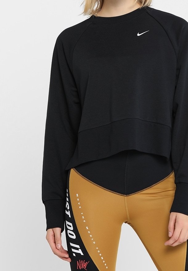 Zwarte cropped sweatshirt met lange raglanmouwen en een wit Nike-logo. Gecombineerd met strakke gouden leggings met witte tekst en accenten.