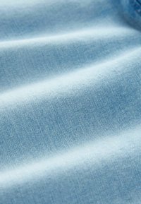 Tessuto in denim blu chiaro con una morbida texture, che mostra delicati motivi di tessitura e pieghe leggere, indicanti flessibilità e morbidezza.