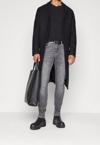 Cappotto nero in lana, camicia nera a maniche lunghe, jeans grigi slim-fit, cintura nera, borsa nera e stivali neri chunky. Tessuto morbido con una vestibilità classica.