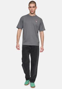 Grå kortærmet t-shirt med et lille logo-patch, parret med sorte lige jeans og grønne sko. Enkel og afslappet design.