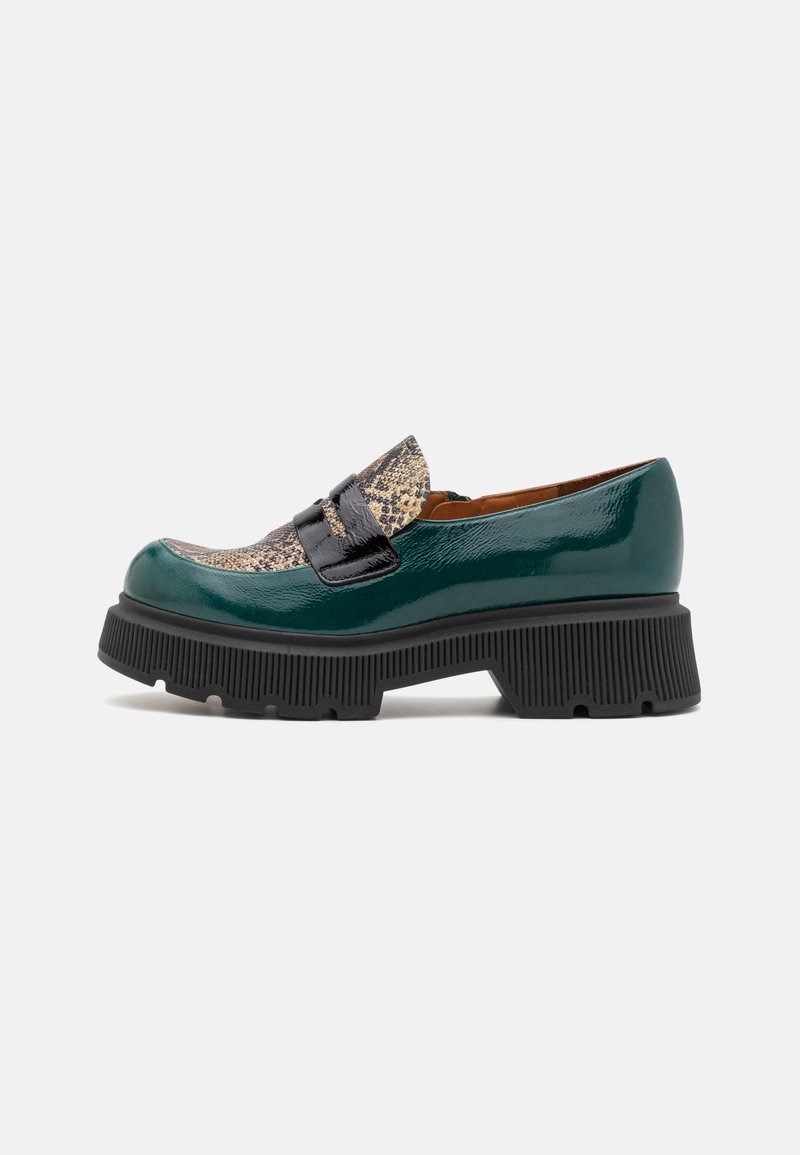 Mocassin vert foncé brillant avec semelle noire épaisse et détail texturé beige et noir sur l'avant supérieur, sur fond uni.