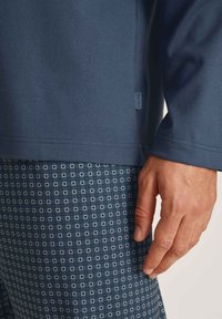 Marineblauwe longsleeve shirt van textuurstof met een label, gecombineerd met gemusterde shorts met kleine witte vierkantjes op een donkerblauwe achtergrond.