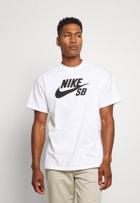 Vitt kortärmad t-shirt i bomull med en stor svart "NIKE SB" logotyp i en djärv design över framsidan.