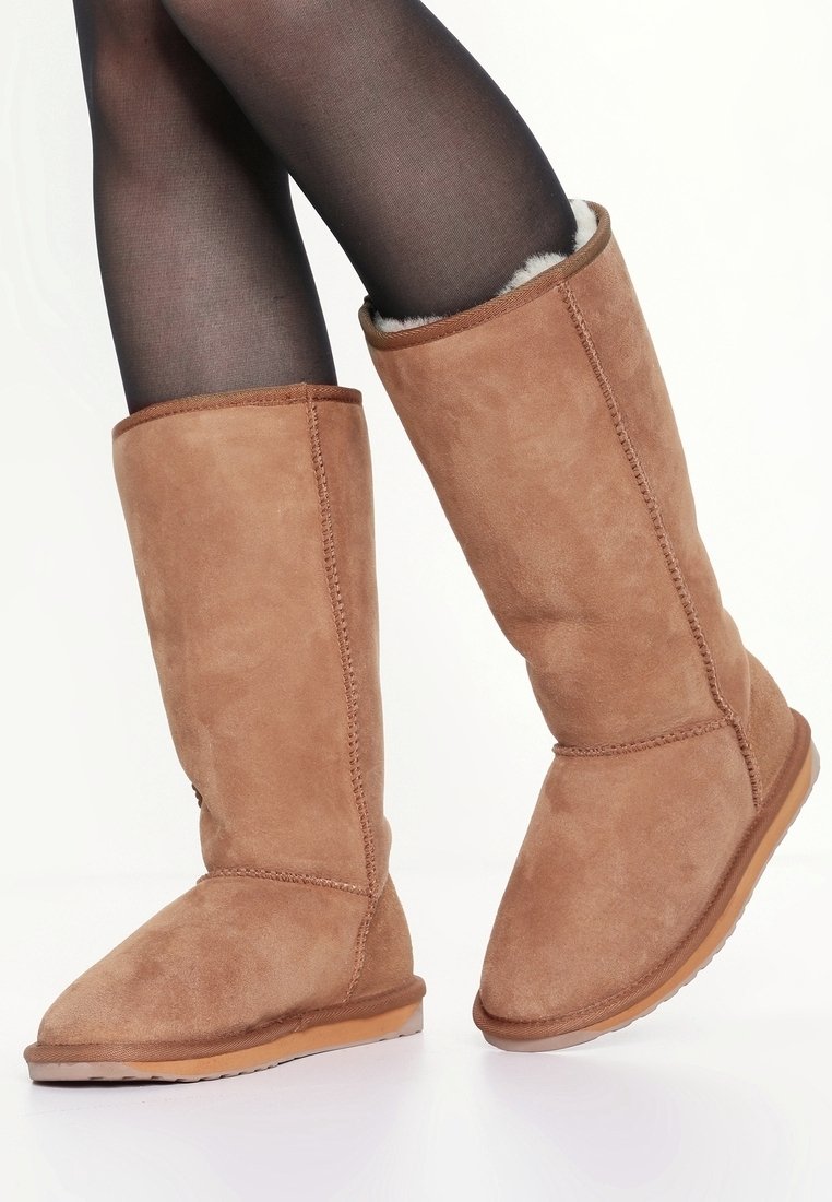 Botas de ante marrón hasta la rodilla con un forro suave, suela plana y punta redondeada, con una costura bordada a lo largo del lateral.