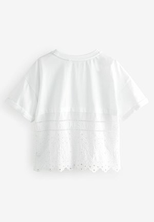 Vit t-shirt med ett lagerutformat design; övre halvan är i slät tyg, nedre halvan har spetsdetaljer med blommönster och scallopade kanter.