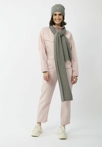 Grijze gebreide beanie en sjaal gecombineerd met een lichtroze jumpsuit en witte sneakers, met een zak aan de linkerkant en een ontspannen pasvorm.