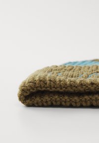 Knit cap in brown with blue accents, featuring a thick, textured weave and a folded edge. The design includes a repeating pattern.