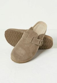 Brown suede clogs with a smooth texture, featuring an adjustable strap and a rubber sole embossed with a wave pattern.
