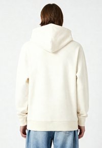 Felpa con cappuccio di colore crema, dal fit rilassato, con polsini e orlo a coste. Texture liscia con una finitura opaca e sottile.