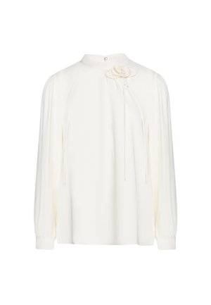 Camicia bianca a maniche lunghe con collo alto e spilla decorativa a forma di fiore sul lato superiore sinistro del petto, con polsini abbottonati.
