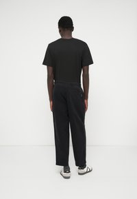 Svart t-shirt och svarta byxor visade från baksidan. T-shirten har en enkel design, medan byxorna har ett elastiskt midjeband och en bakficka.