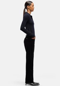 Granatowa koszulka polo z długim rękawem i kołnierzykiem, zestawiona z czarnymi aksamitnymi spodniami i czarnymi spiczastymi butami, prezentująca smukłą sylwetkę.