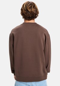 Bruine sweatshirt met een ontspannen pasvorm, lange mouwen en een ronde halslijn. Zachte stof met minimale stikseldetails. Geen zichtbare logo's.