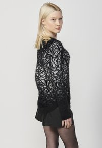 Maglione bianco e nero con una texture morbida, caratterizzato da un motivo geometrico, maniche lunghe e una vestibilità rilassata, abbinato a una gonna nera.