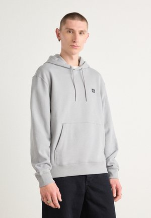 Sudadera gris con capucha, que cuenta con un bolsillo frontal y cordones ajustables. Hecha de una tela suave, tiene puños acanalados y un pequeño parche con el logo.