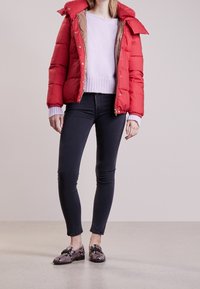 Rode gewatteerde jas met hoge kraag, lichtpaarse trui, donker skinny jeans en geprinte schoenen met een slangenprint en platte zool.