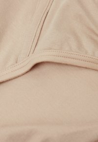 Helles Beige-Gewebe mit glatter Textur, das eine nahtlose Kante und einen dezenten Stretch aufweist, geeignet für angenehmes Tragen.