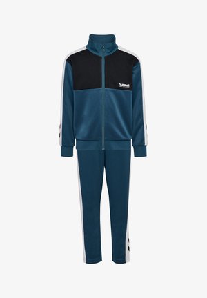 Dreng og pige står side om side iført matchende blå, sorte og hvide træningsdragter med sneakers mod hvid baggrund.