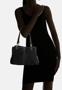 Mustan mokkanahkabagin, jossa on hopeiset yksityiskohdat ja kaksinkertaiset kahvat. Sen pinnassa on teksturoitu viimeistely ja kontrastoivat tikkaukset.