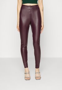 Leggings in eco-pelle bordeaux con un design aderente. Tessuto liscio e vita alta. Abbinati a tacchi a motivi bianchi e neri.