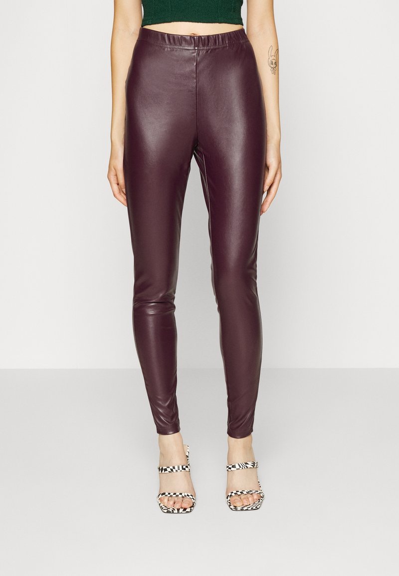 Leggings in eco-pelle bordeaux con un design aderente. Tessuto liscio e vita alta. Abbinati a tacchi a motivi bianchi e neri.