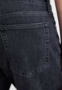Jeans negri din denim cu detalii la buzunarul din spate, prezentând o cusătură subtilă și o suprafață de țesătură texturată. Vedere de aproape, evidențiind forma și designul.