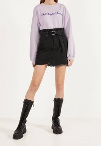 Lila sweatshirt med texten "All Rights Reserved", kombinerad med en svart denimkjol med bälte i midjan och fransar i nederkant. Höga svarta snörkängor.