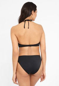 Zwart bikini set met een halternek met strikken, een clasp achterkant en een hoge taille broek. Soepele textuur en minimalistisch ontwerp.