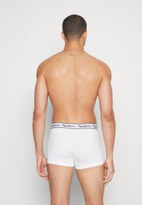 Weiße Baumwoll-Boxershorts mit einem navyfarbenen Logo-Bund, von hinten an einer Person präsentiert, um den Sitz und die Schnittform zu betonen.