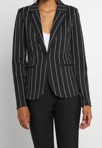 Svart och vit randig blazer med skräddarsydd design, enkel knappstängning, skarpa slag och sidofickor. Slät tygkvalitet.