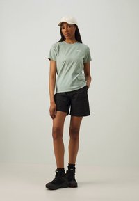 Mündiroheline lühikeste varrukatega t-särk tasku detailiga, kombineeritud mustade cargo lühikestega. Modell kannab beežikat mütsi ja musti matkajalatsid.