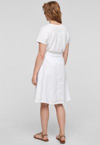 Witte linnen rok met een uitlopende vorm en zijzakken, gedragen met een wit T-shirt. Casual sandalen maken de outfit compleet.