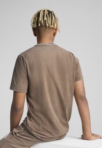 Brun kortærmet t-shirt lavet af blødt stof, med en afslappet pasform og subtil tekstur. Detaljer inkluderer en rund halsudskæring og oprullede ærmer.
