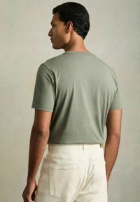 T-shirt verde oliva a maniche corte realizzato in tessuto morbido, abbinato a pantaloni color crema. Presenta un collo a giro e una vestibilità rilassata.