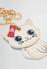 Portachiavi a forma di gatto realizzato in pelle crema, con occhi blu, naso rosa e un fiocco rosso decorato con una gemma. Include accessori color oro.