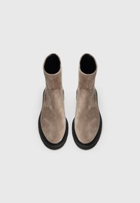 Bottes chelsea en daim beige avec un bout rond et une semelle en caoutchouc noir. Texture lisse et design simple, avec un dessus sans couture et sans matériel visible.