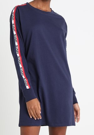 Robe longue pour femmes à manches longues de couleur marine avec une bande logo Levi's en rouge, blanc et noir courant le long des manches, portée à mi-cuisse.