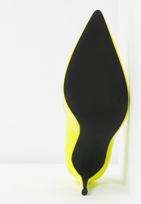 Vue de la semelle d'une chaussure à talon haut jaune à bout pointu avec un talon aiguille fin sur fond blanc.