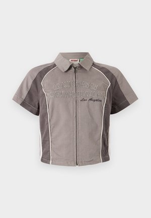 Chemise à manches courtes, à zip sur le devant, de couleur grise avec des accents blancs et le texte brodé "GUESS ORIGINALS Los Angeles". Tissu lisse avec un col structuré.
