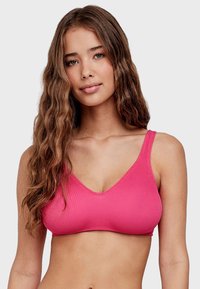 Bralette rosa acanalado con tirantes anchos y escote en V. La tela tiene una apariencia texturizada, ofreciendo un ajuste ceñido.