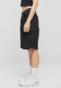 Svarte cargo-shortser med to sidelommer, en rett snitt, og flat linning, sammen med hvite joggesko og ankelsokker.