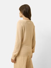 Beiger Strickpullover mit Rundhalsausschnitt, Raglanärmeln und gerippten Bündchen und Saum. Weiche Textur mit minimalen Details auf der Rückseite.