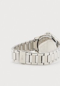 Nerūsošā tērauda pulkstenis ar saistītu rokassprādzes dizainu, kas izceļas ar pulētu apdari un diskrētu iegravētu logotipu sprādzes daļā.