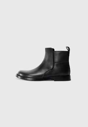 Black leather ankle boot with rounded toe, elastic side panels, and a textured back. Features a flat rubber sole and pull tab.
