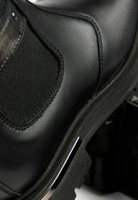 Stivale alla caviglia in pelle nera con pannelli elastici laterali, superiore testurizzato e suola spessa con dettaglio in accento argentato.