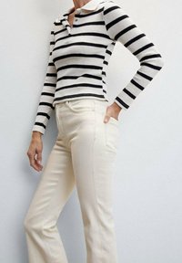 Camiseta de rayas en blanco y negro de manga larga con cuello, combinada con pantalones acampanados de color crema de talle alto con costuras visibles.