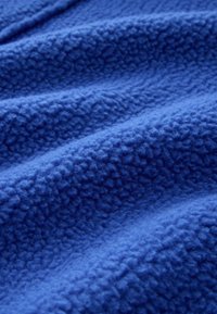 Blå fleece stof med en blød, struktureret overflade. Har et let hævet, ujævnt mønster. Det samlede udseende er glat og rigt på farve.